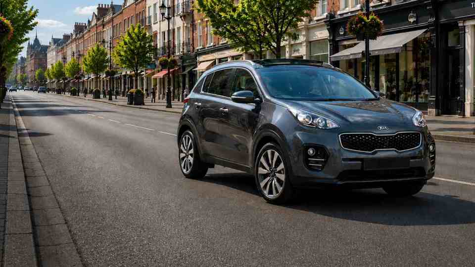 Grey Kia Sportage driving through a town past shops