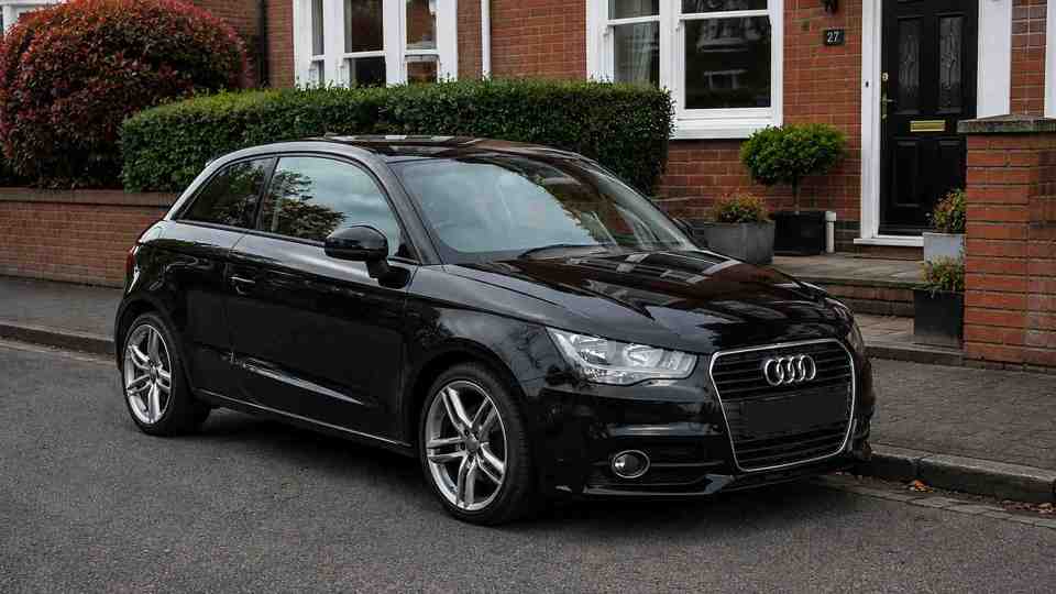 Black Audi A1 parked on road outside a house with a brick wall
