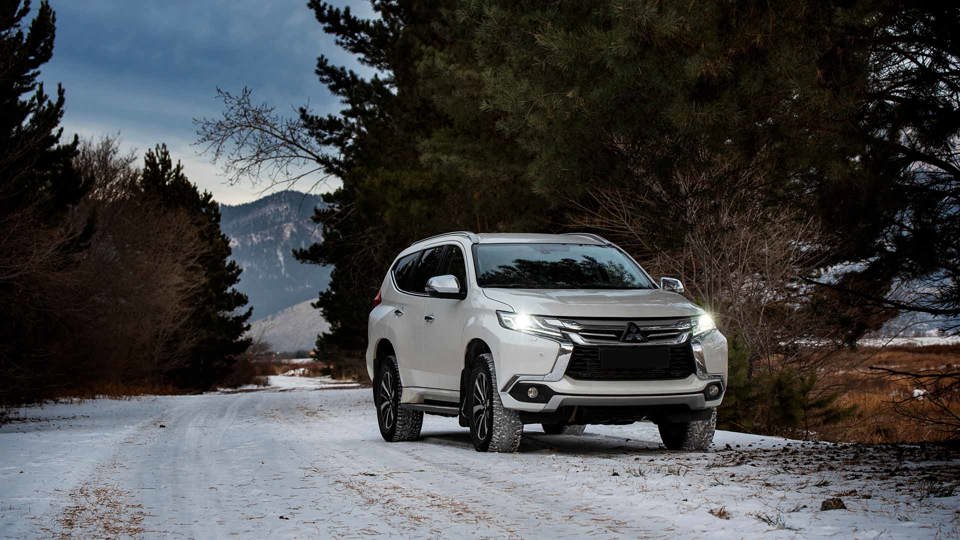 White Mitsubishi driving along a snowy road with pine trees on either side
