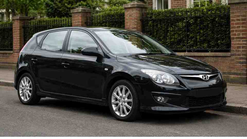 Black Hyundai i30 parked on a street next to a fence