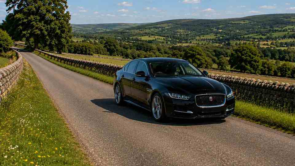 Black Jaguar XE driving on country roads past fields