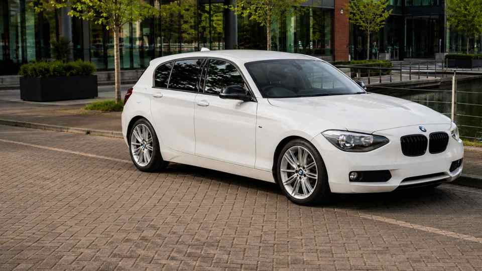 White BMW Series 1 parked by river in a city