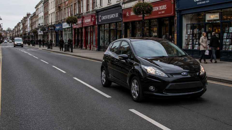 Black Ford Fiesta driving past shops